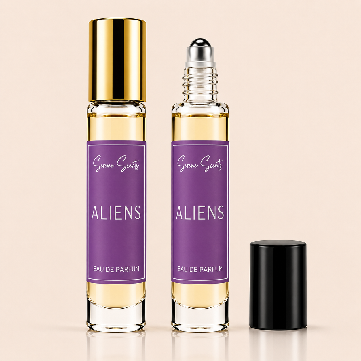 Two clear glass rollerball perfume bottles with purple labels reading 'Space Ghost ALIENS EAU DE PARFUM' are shown on a warm beige background, one with a gold cap and one with a silver rollerball; a black cap sits beside them.