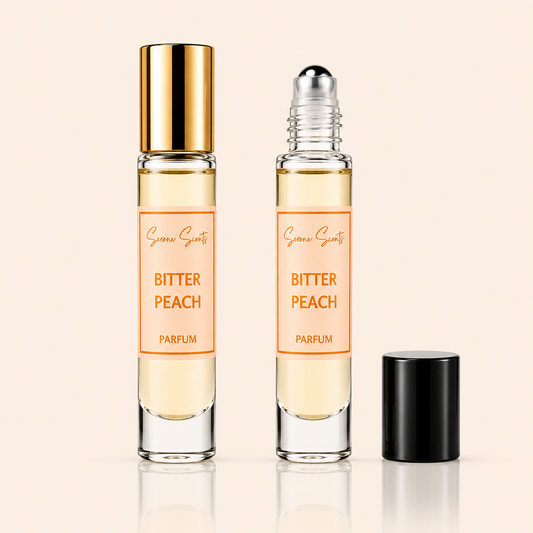 Two glass perfume roller bottles labeled 'Bitter Peach Parfum' by Scenic Scents, shown on a warm beige background. One bottle has a shiny gold cap and the other has a silver roller ball; a black cap sits beside them.