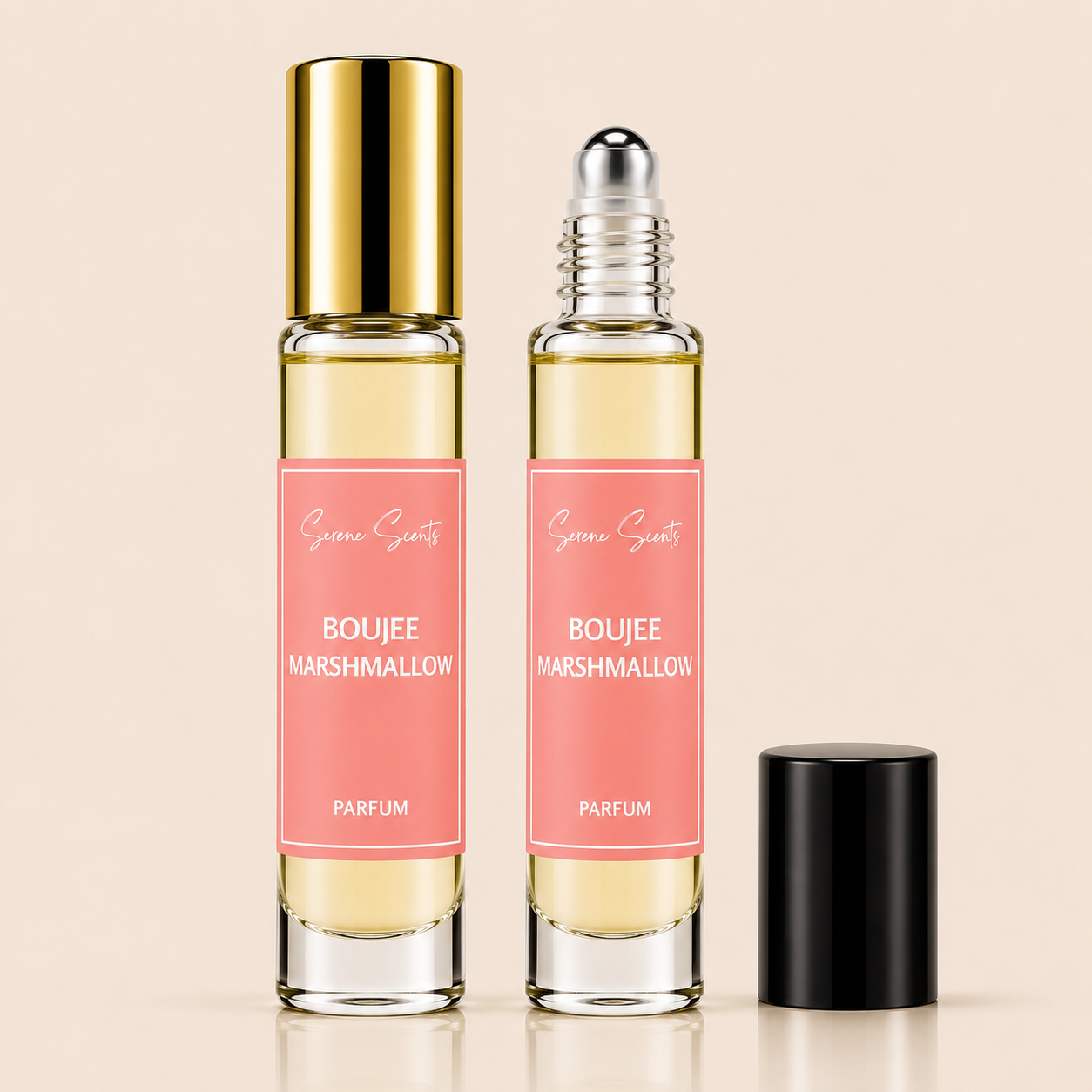 Two clear glass rollerball perfume bottles with pink labels reading 'Boujee Marshmallow Parfum' and 'Scenic Scents,' one with a gold cap and one with a silver cap, plus a separate black cap standing beside them on a light beige background.