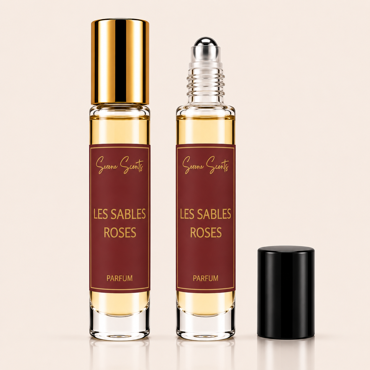 Two clear glass perfume roller bottles with gold caps and dark red labels reading 'Genevies Scentz LES SABLES ROSES PARFUM', shown on a light beige background with one bottle capped and one uncapped showing the roller top.