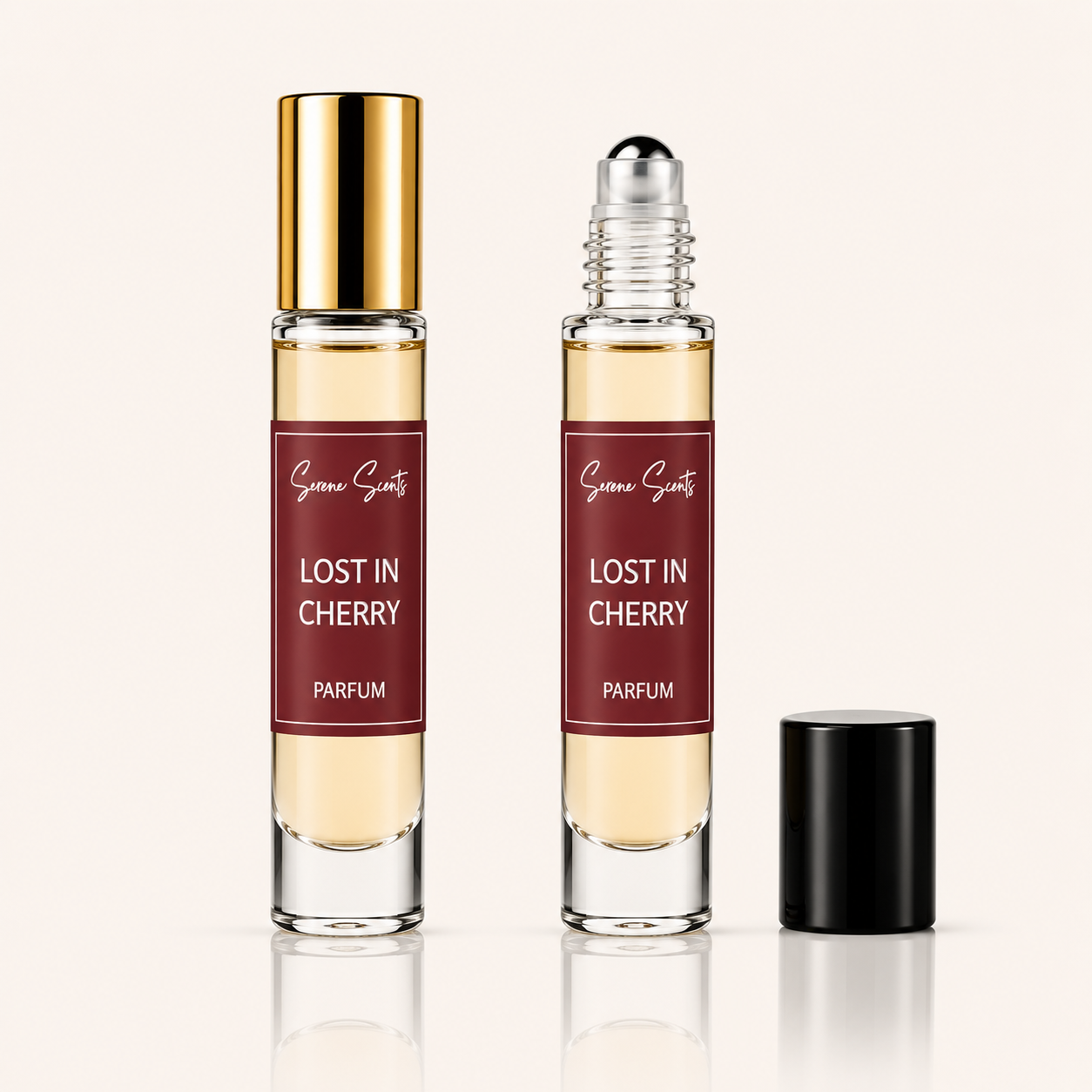 Two clear glass perfume roller bottles labeled 'Scent of Scenery LOST IN CHERRY PARFUM' with amber liquid, one topped with a gold cap and the other with a silver roller ball, with a black cap standing beside them on a light beige background.
