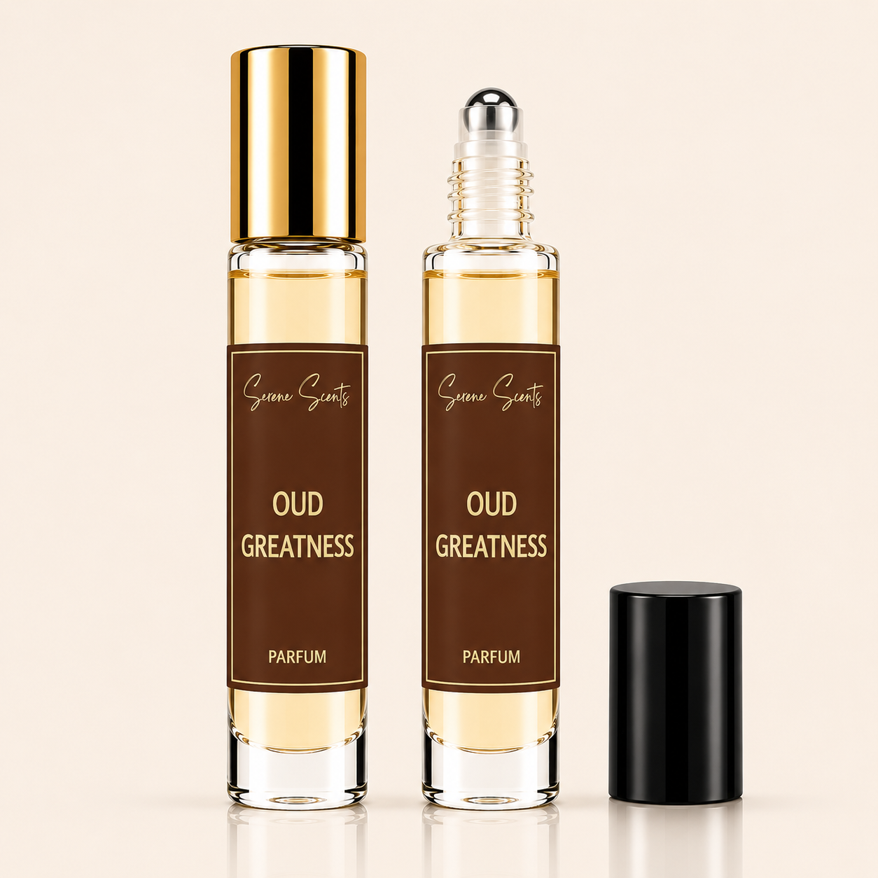 Two clear glass perfume roller bottles with amber liquid, brown labels reading 'Oud Greatness Parfum,' and one black cap, shown on a light beige background.